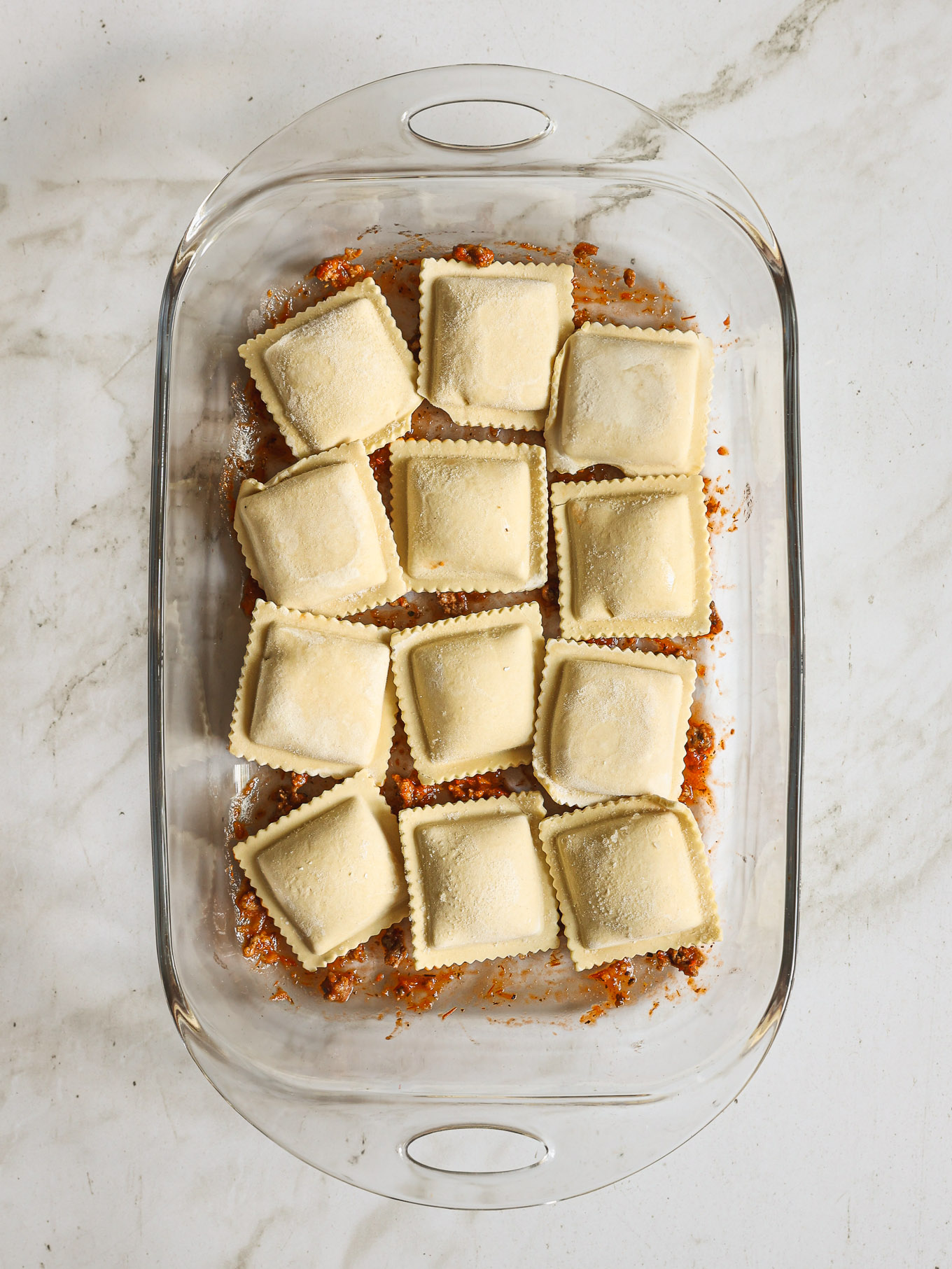 ravioli layered over meat sauce in a baking dish.