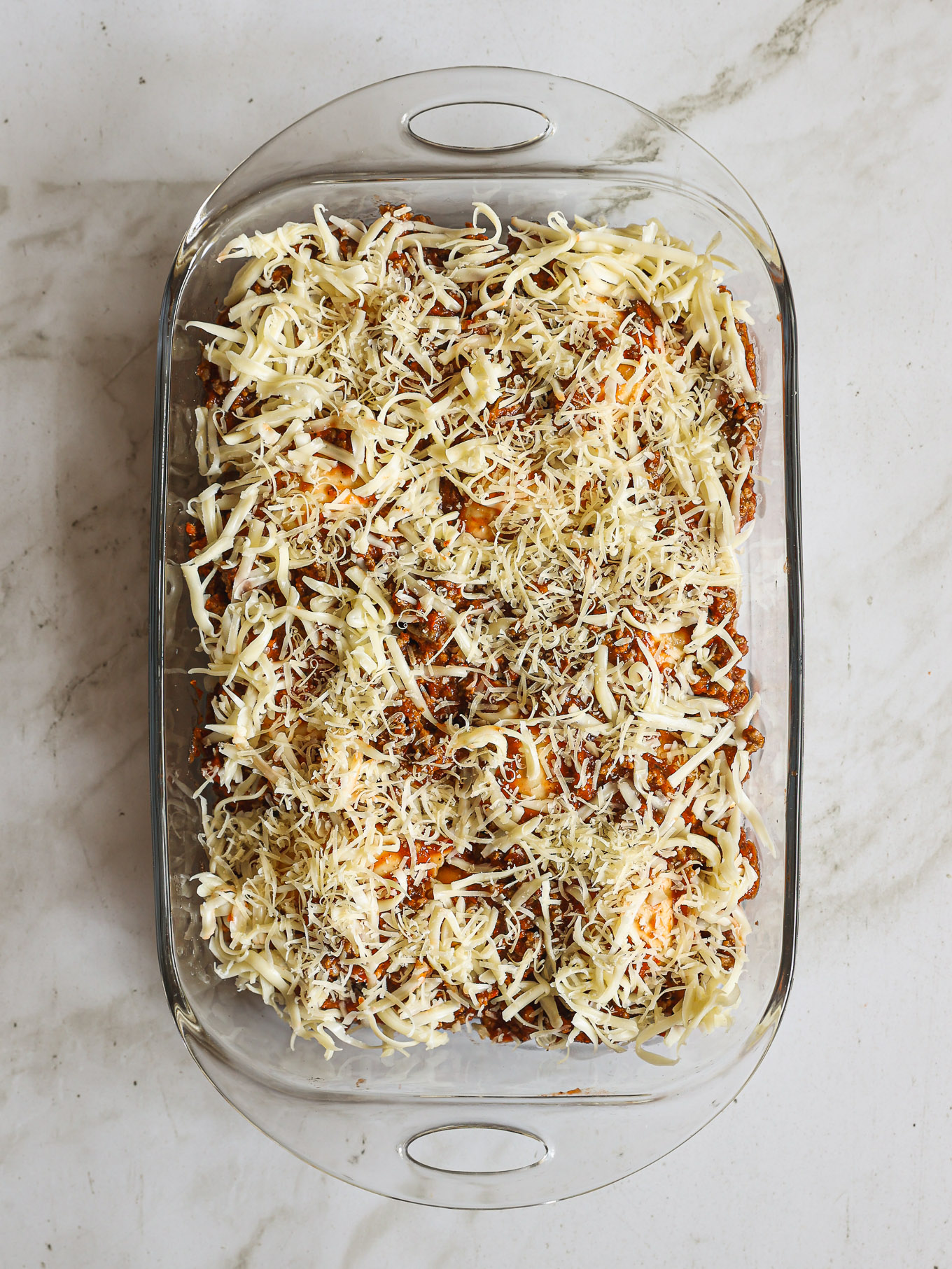 ravioli bake in a glass baking dish topped with cheese and spices.