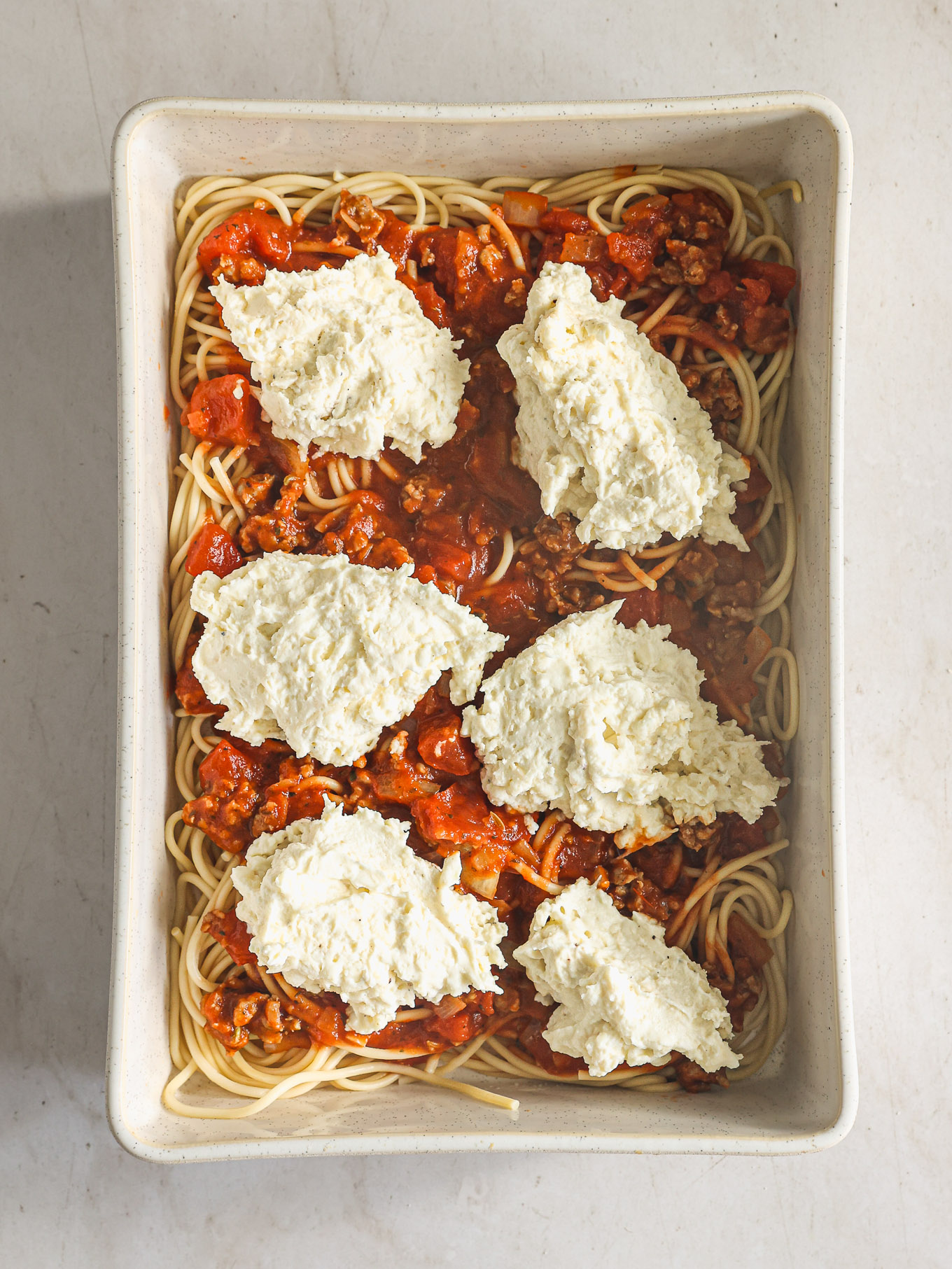 spaghetti in a casserole dish topped with meat sauce and ricotta.
