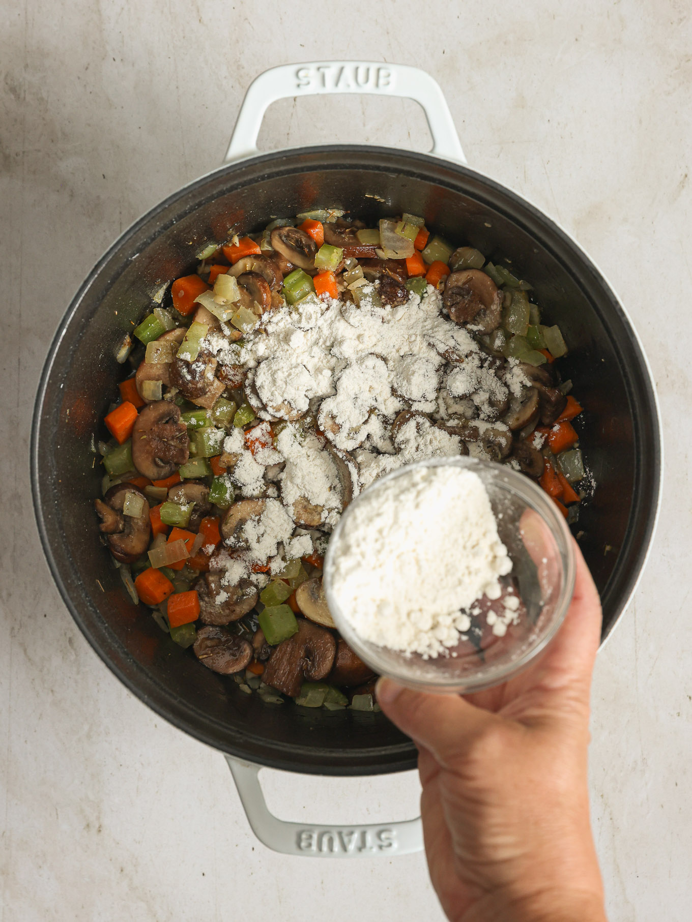 flour sprinkled over cooked vegetables in a soup pot.