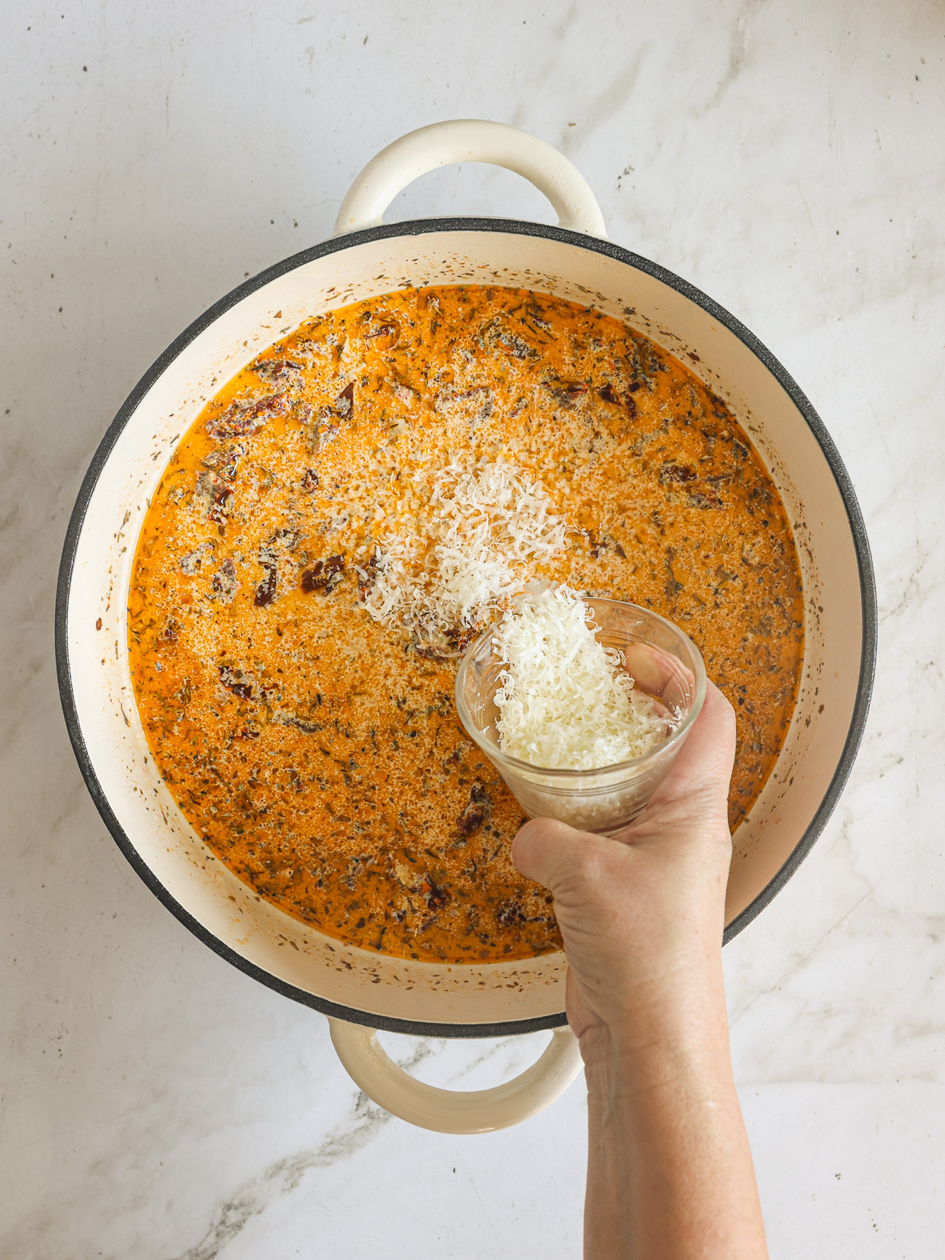 parmesan going into a pan with sauce.