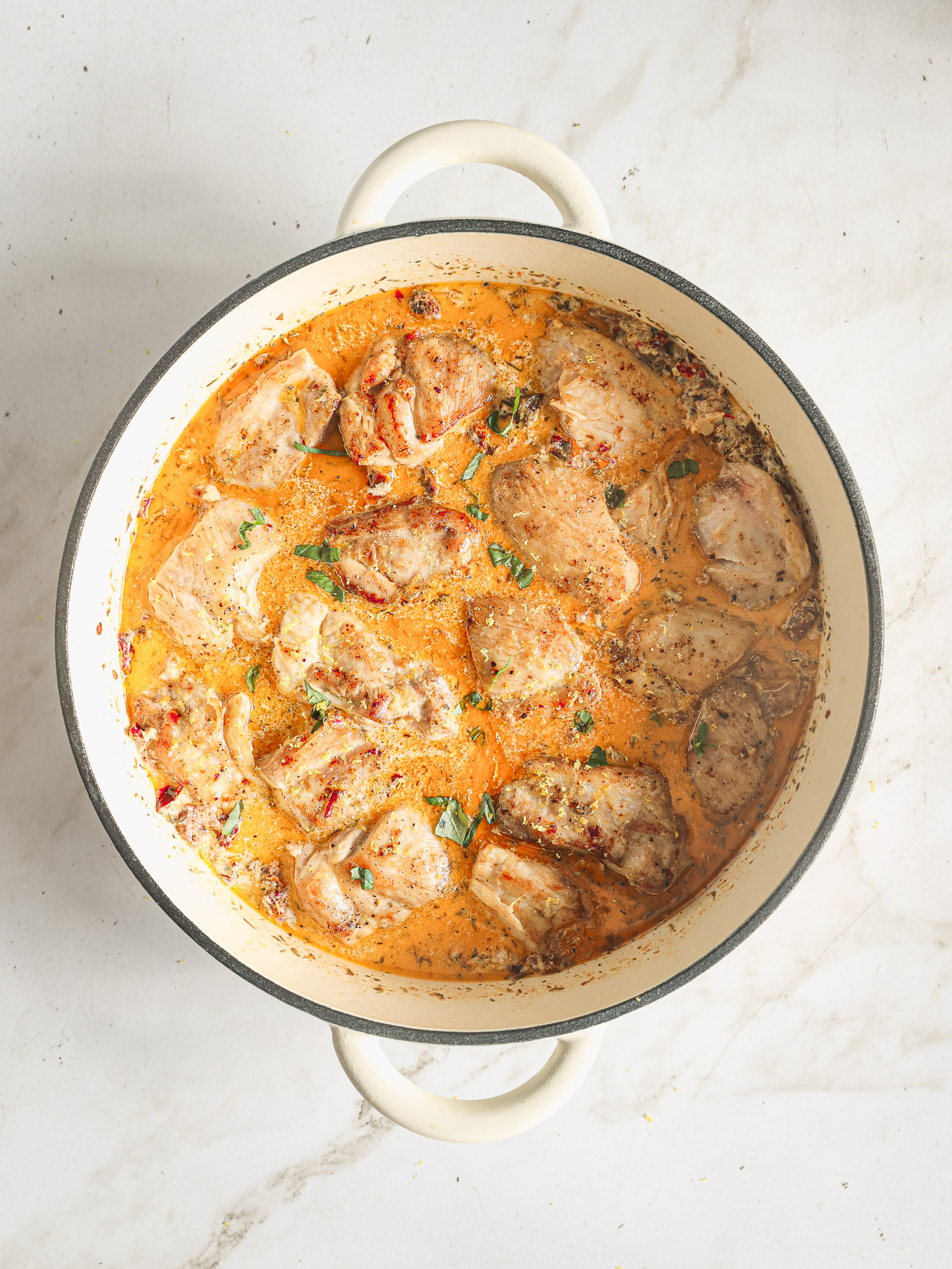 chicken pieces in cream sauce in a pan.