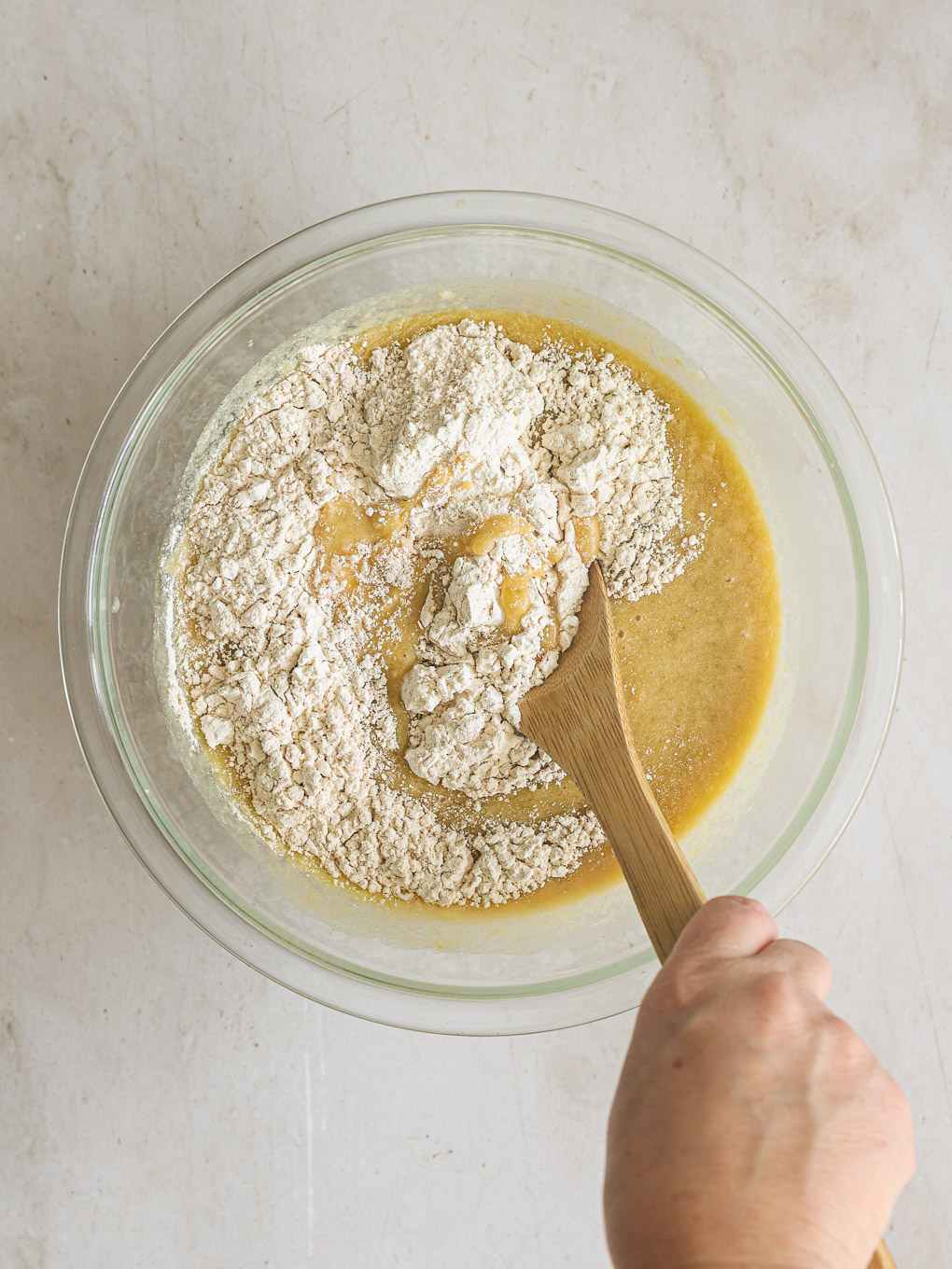 dry and wet ingredients in glass bowl with spatula.