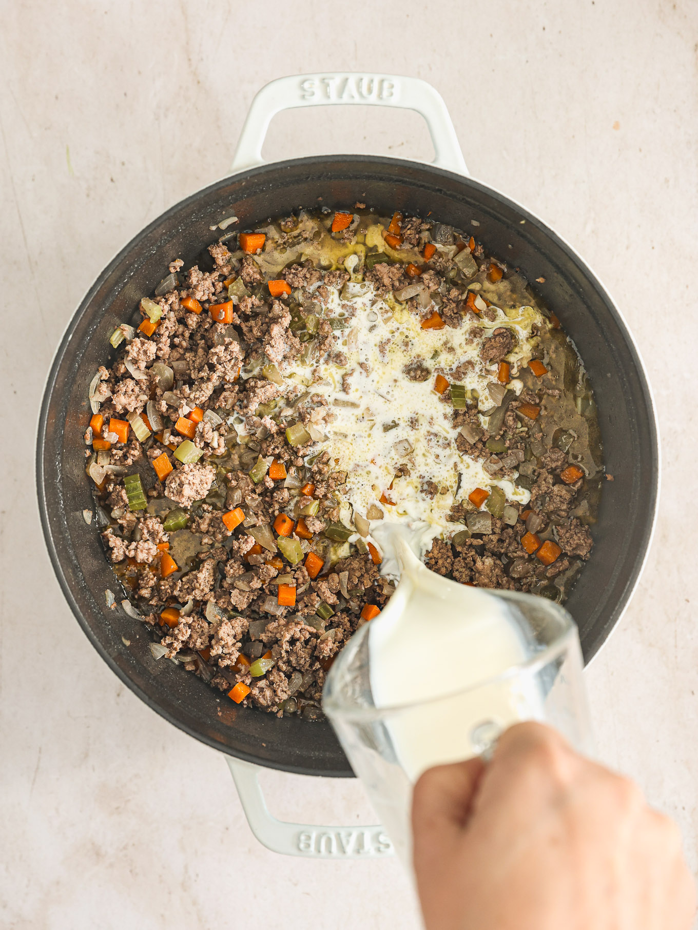 milk poured into a pot with meat and vegetables.