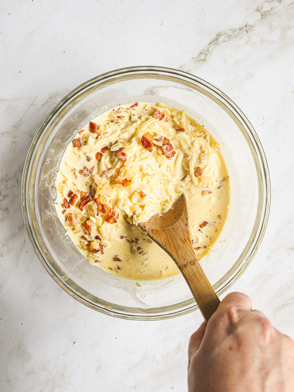 whisked eggs with cooked bacon and onions in a glass bowl.