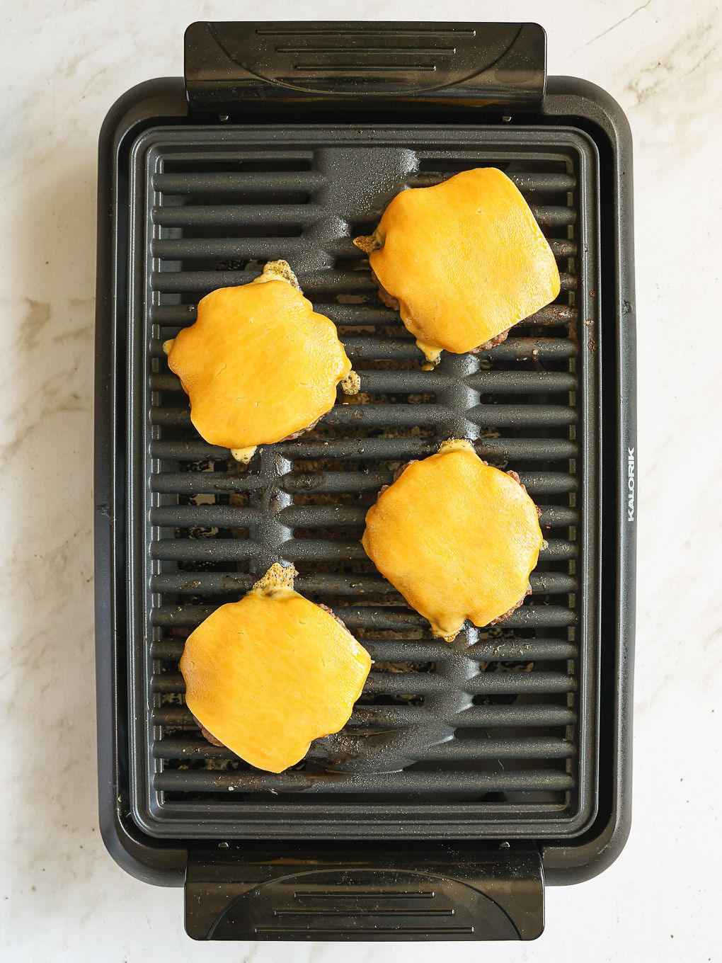 cooked beef patties on a griddle with cheese on top.