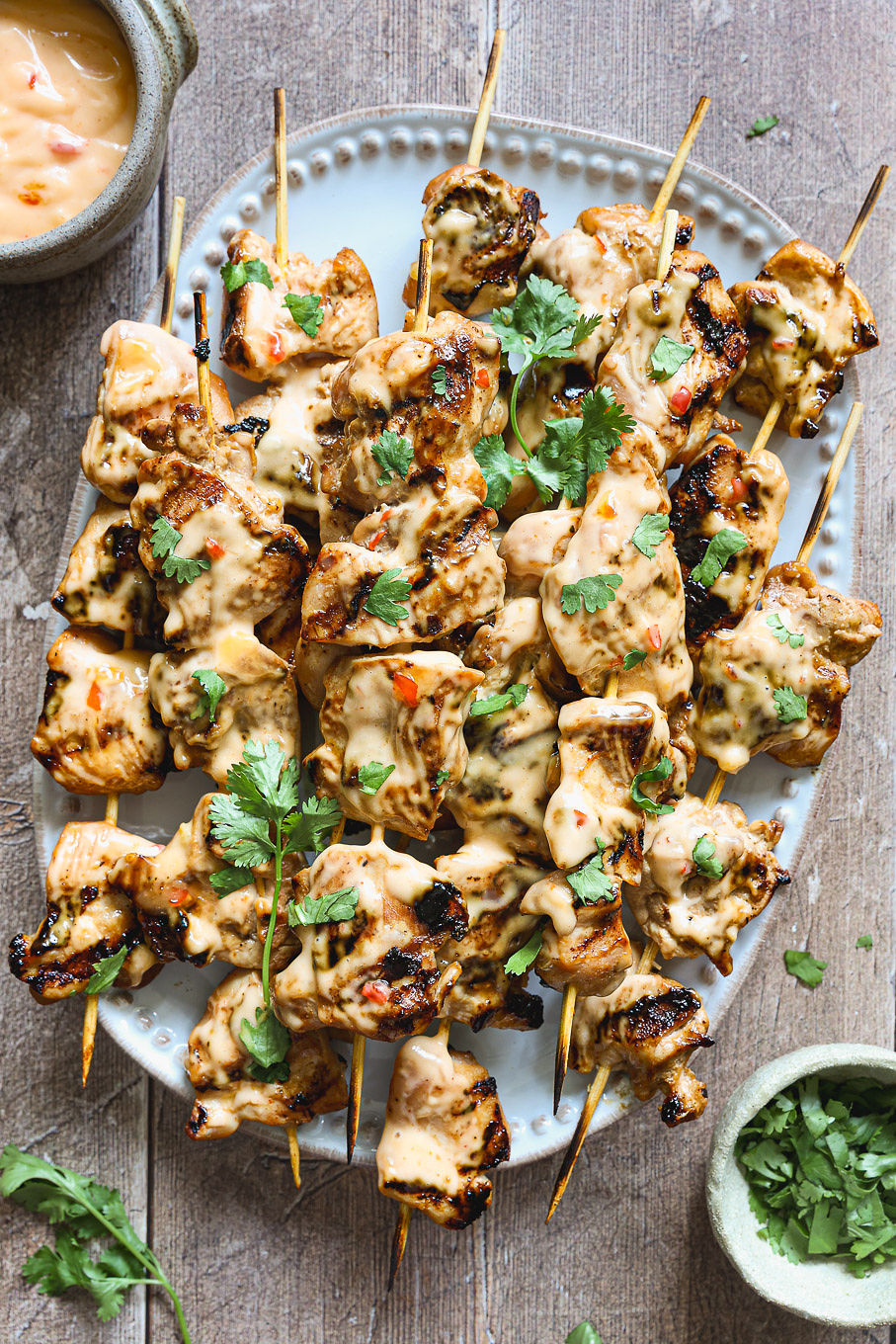 bang bang chicken skewers on a platter with sauce.