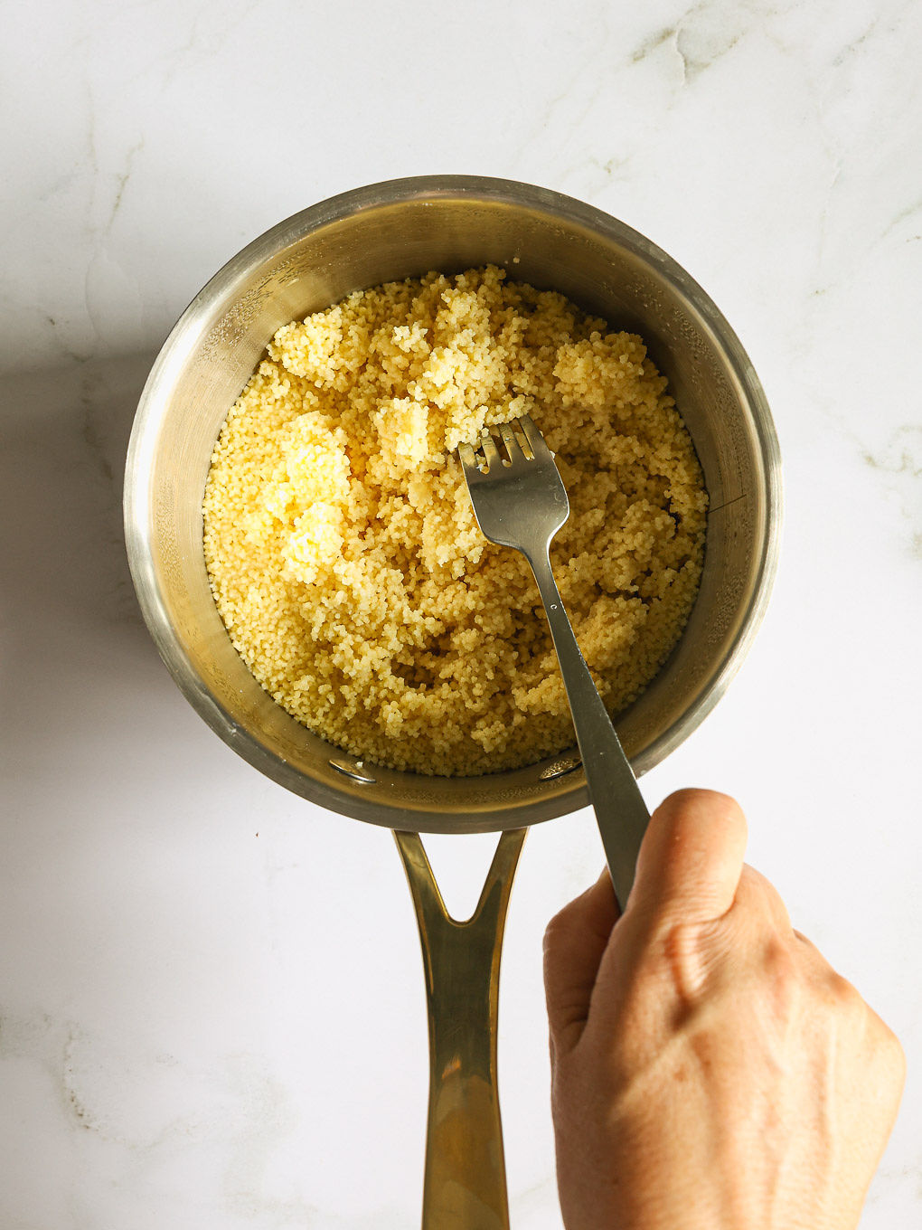 cooked couscous fluffed in a pan.