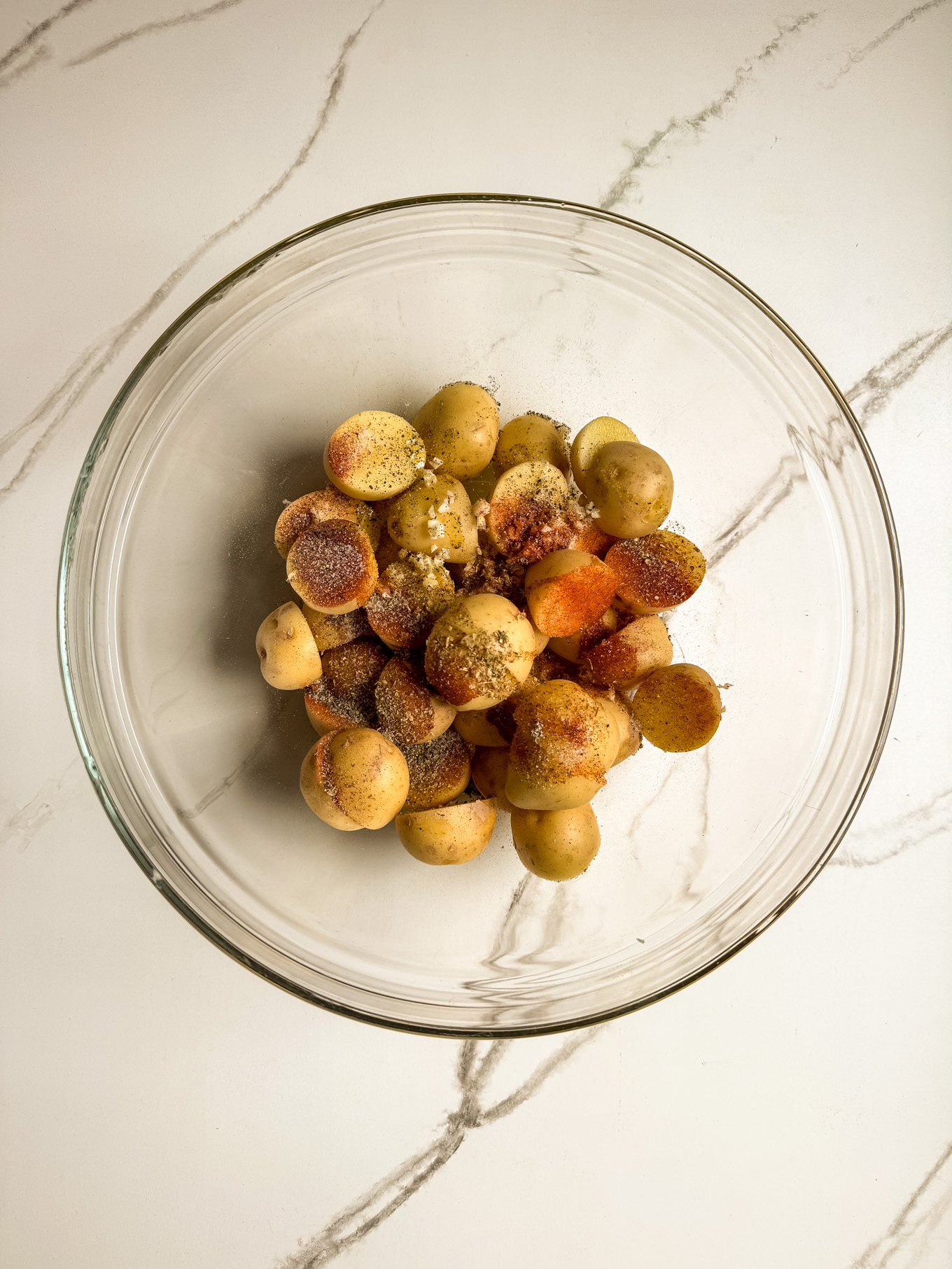 halved potatoes with spices in a glass mixing bowl.