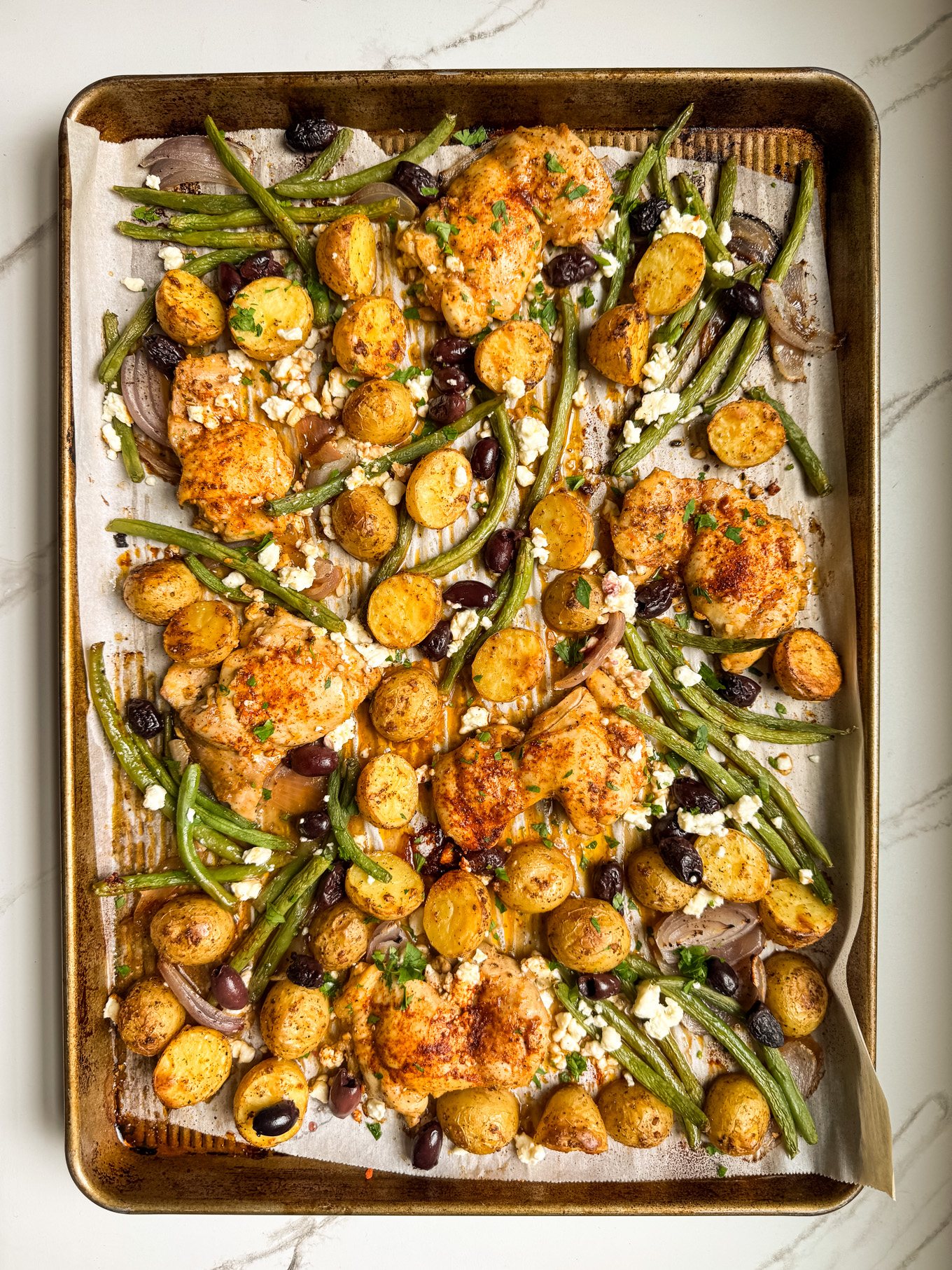 roasted chicken with potatoes, green beans, olives, and feta on a sheet pan.