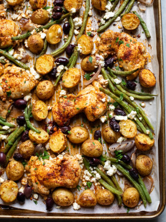 close up roasted chicken with potatoes and green beans on sheet pan.