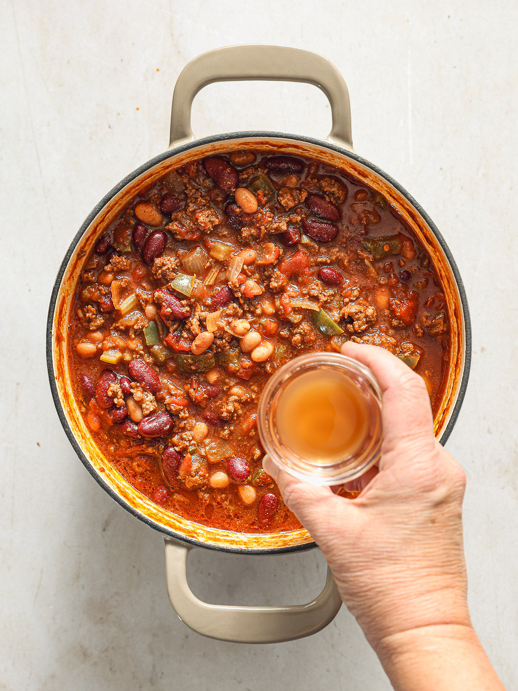 cooked beef chili in a pot with bowl of vinegar going in.